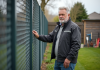 Homme inspectant une cloture métallique moderne dans un jardin