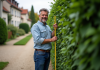 Normes pour les haies : quelles règles respecter en France ? Homme mesurant une haie dans un jardin en banlieue